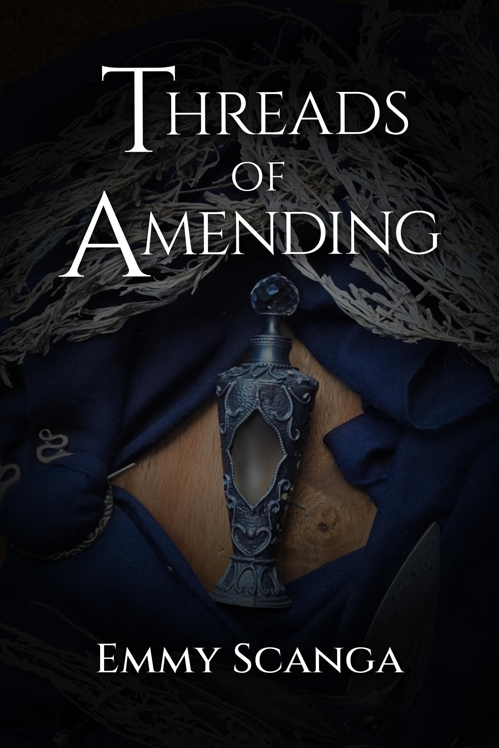 Photo of the cover of Book Two of the Fate Weavers Collection: Threads of Amending by Emmy Scanga. On the cover is a vintage vial in the center of a wood surface surrounded by sagebrush and a navy scarf.